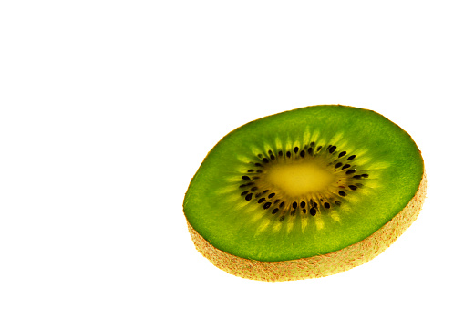 kiwi slice against light, close up view, green color fruit on white background, space for text