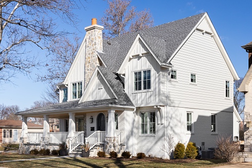 Naperville, IL, USA - February 12, 2024: A beautiful white modern farmhouse with a covered front porch, rock covered chimney, and board and batten siding.