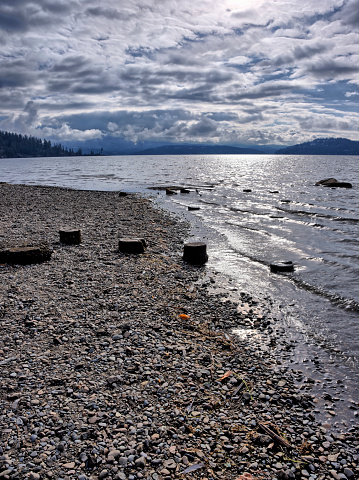 The stone covered  beach and old post stumps by the rippled water of Lake Coeur d'Alene in north Idaho.
