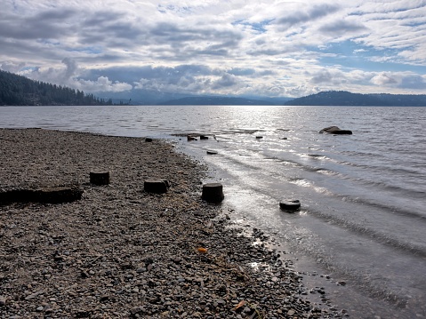The stone covered  beach and old post stumps by the rippled water of Lake Coeur d'Alene in north Idaho.