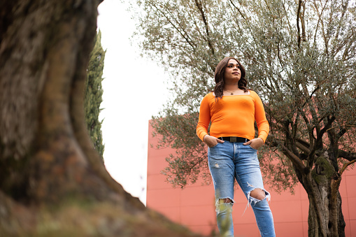 View from below of trans woman in orange shirt in park. Selective focus, copy space. High quality photo