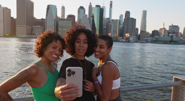 Three women friends shoot a selfie in front of New York skyline at sunset