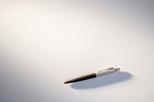 Simple yet elegant classic ballpoint pen resting on a pure white paper, symbolizing potential creativity or work.