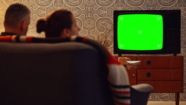 LD Couple sitting on the sofa and watching an old TV set with a green screen
