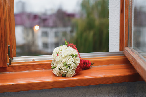 The bride's wedding bouquet of white roses lies on the windowsill