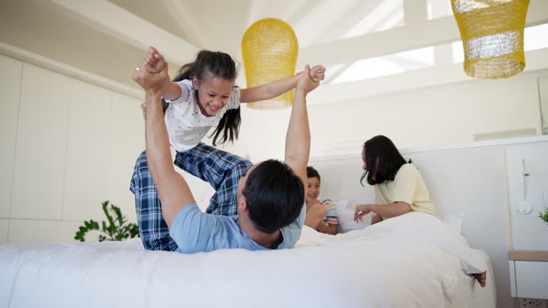 Father, girl and family in bedroom for airplane games, excited or holding hands for safety in house. Parents, children and lift with smile, love and comic playing for morning on bed, holiday and home