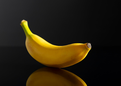 Ripe juicy banana on a black reflective background.