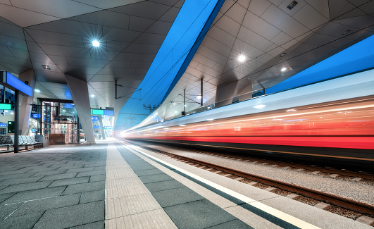 High speed train in motion on the railway station at night. Fast moving red modern intercity passenger train, railway platform with illumination. Modern train station in Vienna, Austria. Railroad