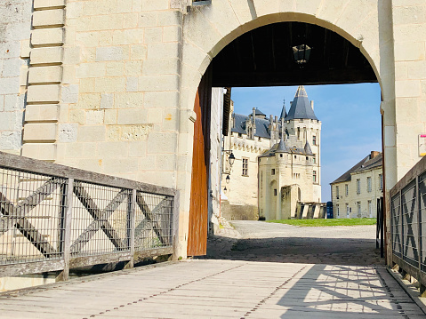 Horizontal closeup photo of the curved entryway and wooden bridge leading to the courtyard and stone buildings of the Chateau de Saumur on the hilltop above the town of Saumur and the Loire River. Maine-et-Loire department, France. 1st April, 2019.
