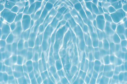 Water surface. Bluewater waves on the surface ripples blurred. Defocus blurred transparent blue colored clear calm water surface texture with splash and bubbles. Water waves with shining pattern.