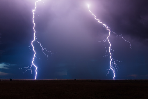 A pair of powerful lightning bolts strike from a thunderstorm, illuminating the night sky near House, New Mexico.