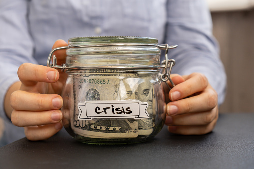 Female hands holding Glass jar full of American currency dollars cash banknote with text CRISIS. Preparation saving money. Moderate consumption and economy. Collecting money