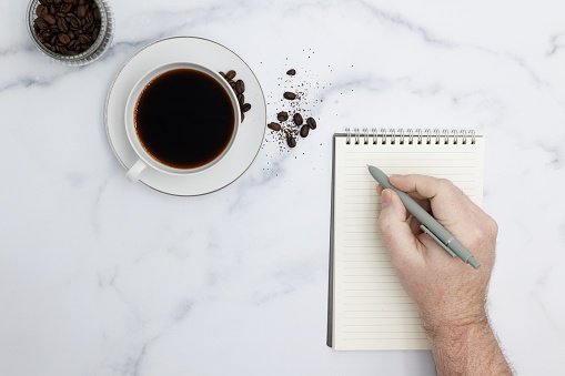 Hand writing on notepad with black coffee cup and beans.