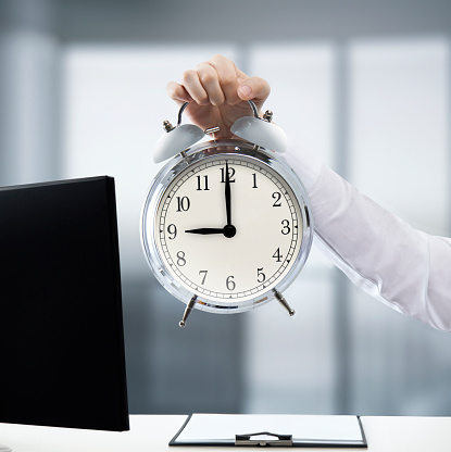 Businessman holding an alarm clock in a modern office showing 9 o’clock