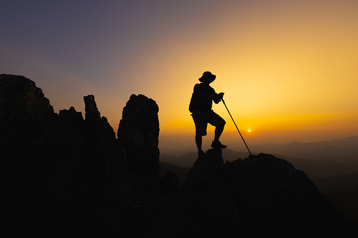 Silhouette of a Climber at the top of the rocky mountain at sunset, Man on top of mountain. Conceptual design. alone at the summit climber  successful climbers. Sport and active life.