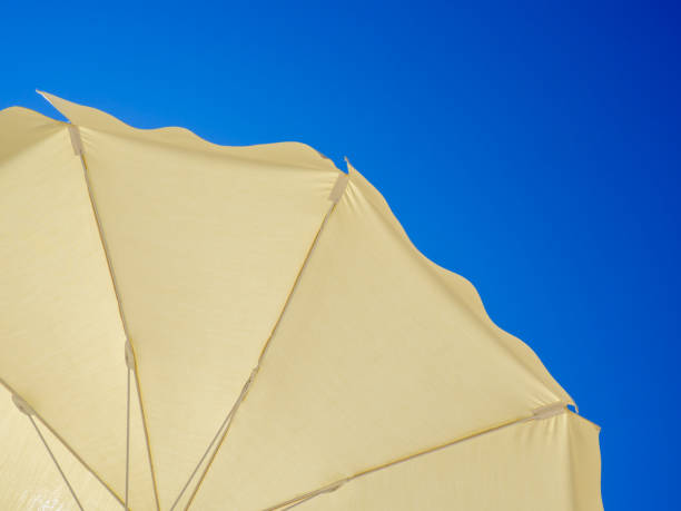 White beach umbrella. Blue sky in the background. View from below. Relaxing context. Summer holidays by the sea. General contest and location