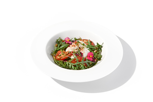 Italian salad with burrata, tomatoes, and arugula, elegantly arranged and garnished with edible flowers.