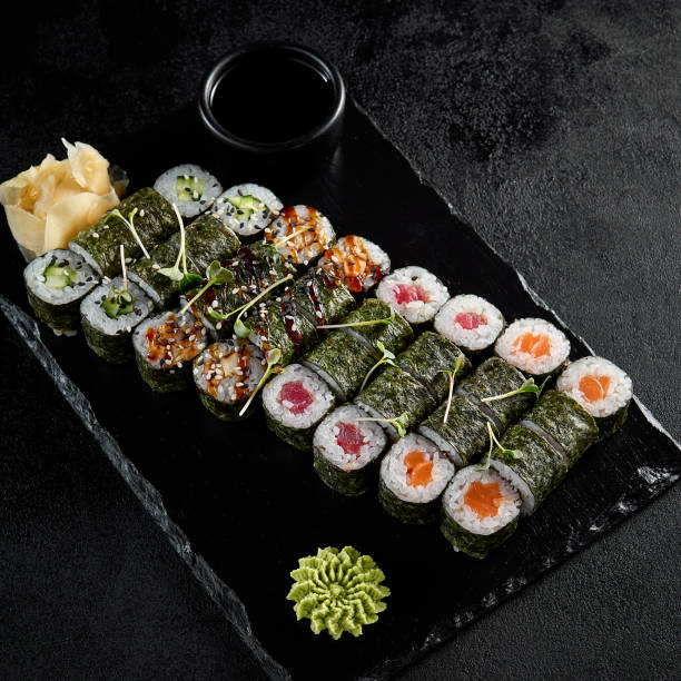 istock Assorted hosomaki sushi set with salmon, tuna, eel, and cucumber on black textured background 2009429614