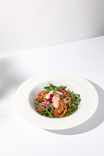 Italian salad with burrata, tomatoes, and arugula in shadow, garnished with edible flowers.