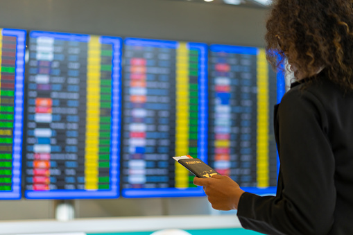 African businesswoman looking flight schedule on timetable and go to check-in counter and boarding gate in airport terminal. Business people travel by airplane transportation on holiday vacation.