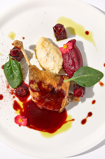 Duck leg confit with berry sauce on a white background, top view - a gourmet delight for fine dining establishments.