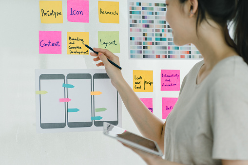 young asian designer brainstorming app interface with colorful sticky notes