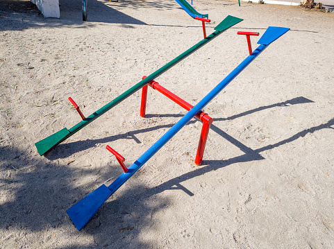 Two seesaws in a playground for children's toys. A green seesaw and a blue one