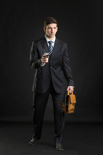 Young man in formal wear holding brown leather bag on black background in studio