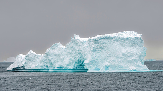 Huge Iceberg floating on Antarctic Ocean at the Coast of Antarctica Peninsula under overcast sky. Antarctica Ocean, Coast of Antarctica.