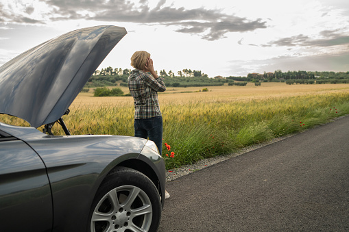 Mature woman having car problems during road trip through countryside