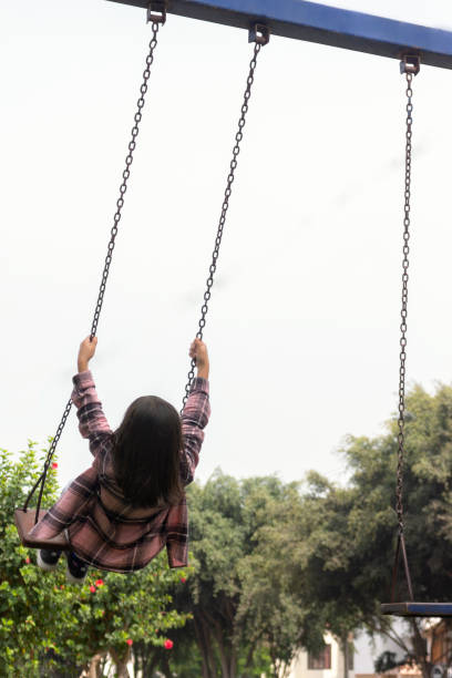 Little girl playing on a swing in a park on a cloudy day, low angle image