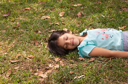 Eight-year-old girl smiling lying on the grass surrounded by leaves and illuminated by natural light on a spring day
