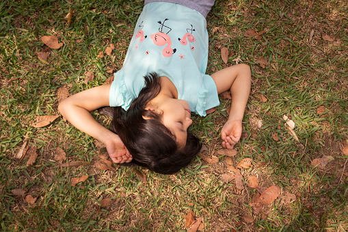 Eight-year-old girl smiling lying on the grass surrounded by leaves and illuminated by natural light on a spring day