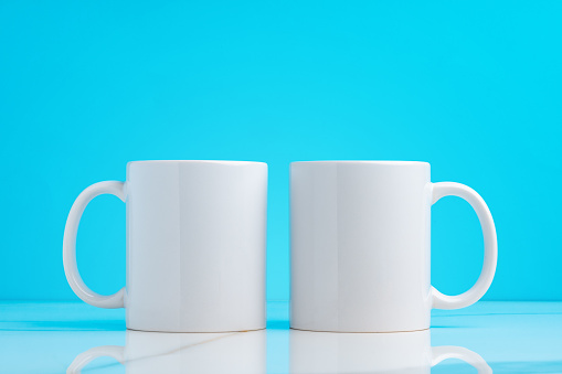 Two ceramic mugs on blue studio background close up