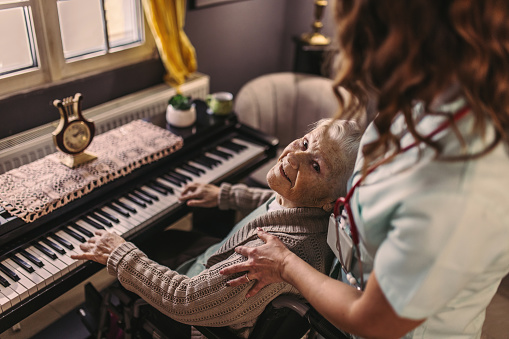 at home, the nurse listens to the senior woman playing the piano
