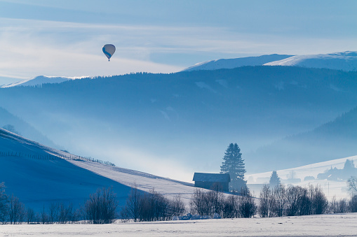 A hot air balloon floating over snow-covered mountains and valleys