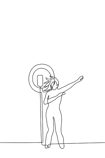 woman shoots dance vertical video on telephone mounted on rack with ring lamp - one line drawing vector. concept female blogger creates content; woman makes dub move to camera