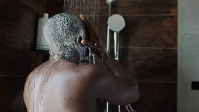 Young Black Man Washing Hair with Shampoo in Shower