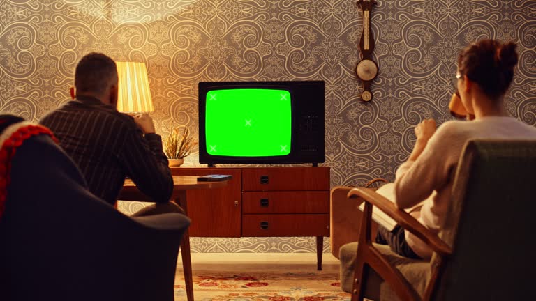 LD Couple drinking tea and watching an old TV set with a green screen in the living room