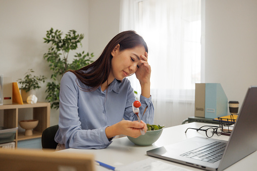 Young beautiful woman experiencing headache while having breakfast at home office