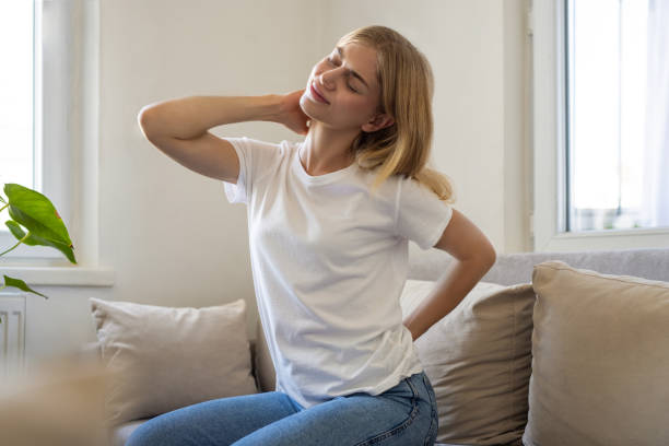 Worried woman sitting on sofa at home and touching her back