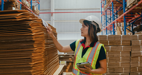 Young Asian woman warehouse worker checks stock and inventory with digital tablet in factory warehouse. Logistic industry business concept.