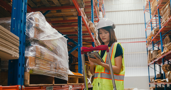 Young Asian woman warehouse worker checks stock and inventory with digital tablet in factory warehouse. Logistic industry business concept.