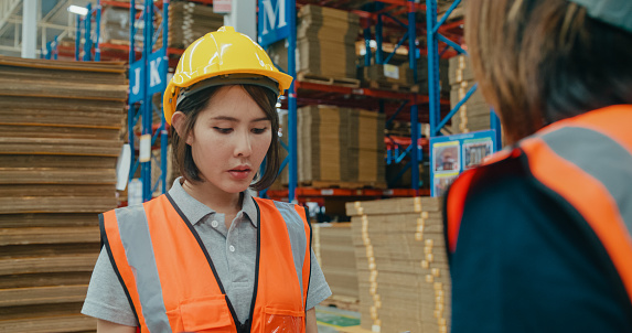 Young Asian women worker checks stock inventory with tablet and laptop and discuss talk together in retail warehouse. Logistic industry business concept.
