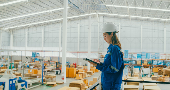 Professional Asian female industrial engineers use tablet while standing in manufacturing factory. Working in manufacturing plant or production plant concept.
