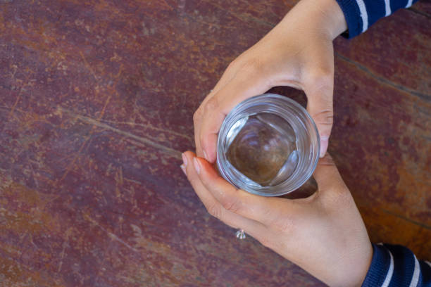 Top view a hand catching glass of pure water on the wooden table, healthcare and refreshment concept, copy space for text