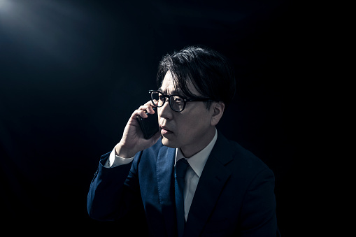 Businessman in Suit Making Phone Call on Smartphone in Dimly Lit Room