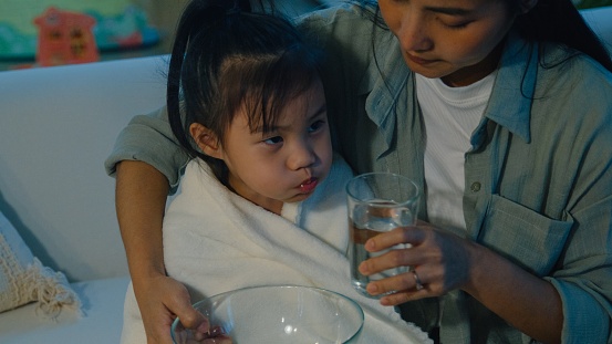 Mom takes care of her daughter who gets sick and has a high fever and lets her child do the mouthwash in the nighttime at home. Illness Girl with a medical condition and family wellness concept.