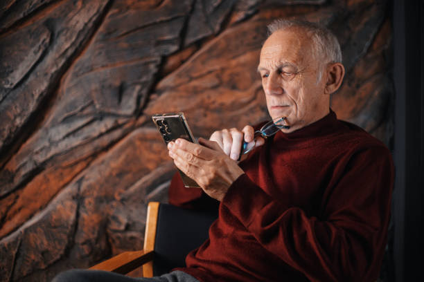 istock Pensive old man sitting in a chair typing a message on his phone 2009732989