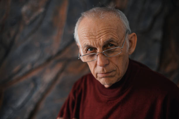 Old man with glasses looks seriously at the camera